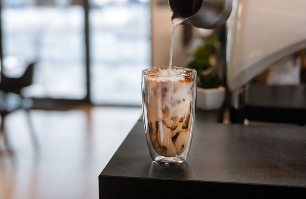 Un iced latte al que se le está echando leche, un cremoso bebida de café en verano